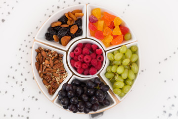 Round set of plates full of nuts, raspberries, sweets, grapes and dry fruit on the white background. Healthy snacks. Desserts for  coffee or tea. Assorted mix of pecans, berries and fruit.