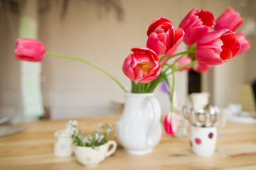 Beautiful table setting with red tulips, forget-me-not and cups on the wooden table.