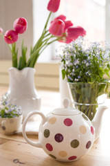 Obraz na płótnie Canvas Teapot with dots and vases with beautiful spring flowers on the wooden table. Decoration for home interior. Forget-me-not and tulips in vases. Flowers from the garden.Tea time and table setting.