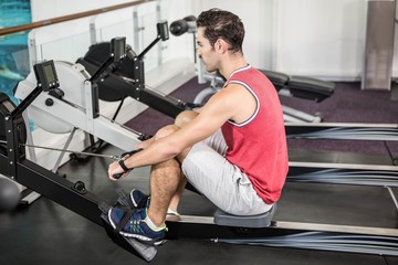 Obraz na płótnie Canvas Muscular man on rowing machine