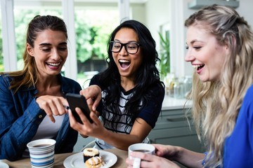 Female friends laughing while pointing on mobile phone