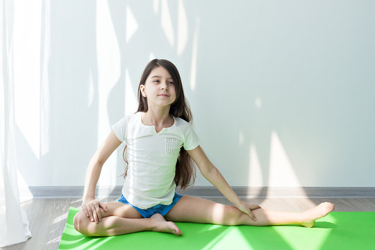 little girl doing gymnastics on a green yoga mat doing fitness exercises and stretching. children's fitness and yoga for children.