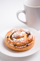 close up of sweet bun with raisins and cup of coffee over white