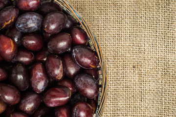 Fresh prune plums in basket on canvas background..