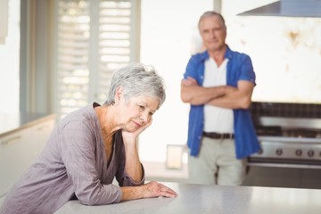Worried senior woman sitting with man standing in background