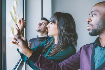 Three business people having a meeting in office. They are standing in front of glass wall with...