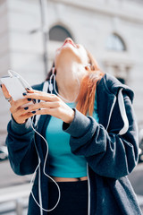 Half length of young handsome caucasian reddish hair woman listening music with earphones, smart phone handhold, laughing - relax, music, technology concept