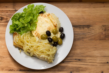 cod fish with onion and mashed potato on white plate on brown wooden background