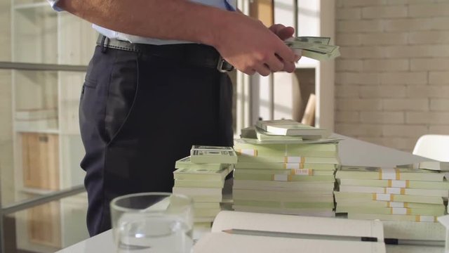 Man standing in the architect office, counting stacks of money and throwing them on the table