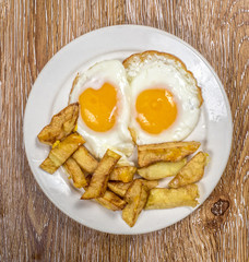 Breakfast with fried eggs and french fries on wooden background
