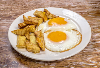 Breakfast with fried eggs and french fries on wooden background