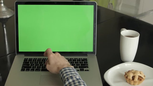 A man types on a laptop on his desk.  Green screen for your custom screen content.