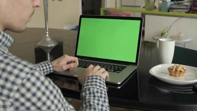 A man types on a laptop on his desk.  Green screen for your custom screen content.