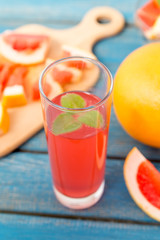 Freshly squeezed orange and grapefruit juice in glass, with fruits on wooden background