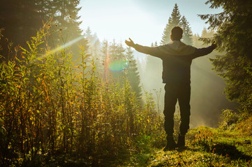 Happy man with hands up on the mountain in the rays of sun.