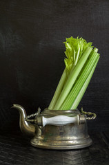 Dark food background with old metal kettle and fresh celery.