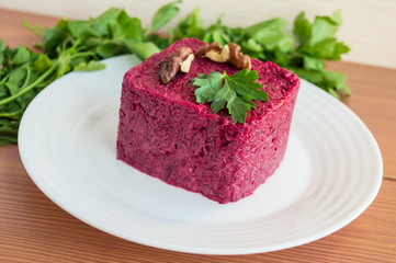 Vitamin salad of boiled beets in the form of a square, with walnuts on a white plate