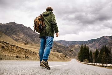 a man with a backpack walks alone on a mountain road
