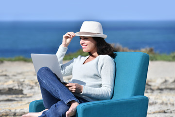 Woman using laptop by the sea, sit in armchair