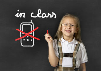 young sweet junior schoolgirl writing with chalk about not using mobile phone in school class