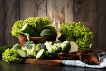 Fresh broccoli, cucumber and salad on black stone with wooden background