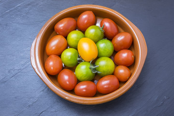 red, yellow and green tomatoes in a bowl on a table slate
