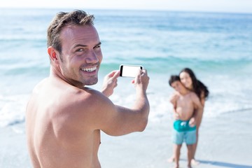 Man smiling while photographing wife and son at sea shore
