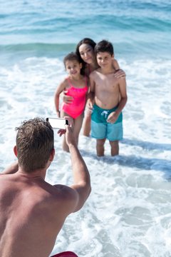 Man photographing children and wife in shallow water