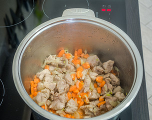 Stainless steel iron pot on an induction cooker which prepares the meat with onions and carrots for cooking pilaf