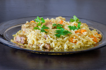 Glass plate on black table with pilaf with meat pork and spices