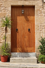 Fototapeta na wymiar wooden door in stone wall decorated with flowers, mediterranean