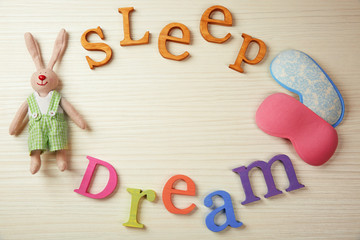 Text Sleep Dream, masks and rabbit toy on light wooden table, top view