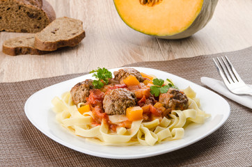Meatballs with pasta, pumpkin and vegetable sauce on a white plate, wooden table, close-up