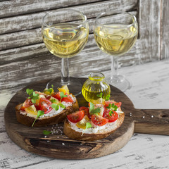Tomato and cheese bruschetta and two glasses of white wine on a rustic wooden cutting board. Healthy breakfast, snack or appetizer with wine