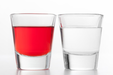 Two glasses of alcohol. One red flavoured, the other clean vodka.