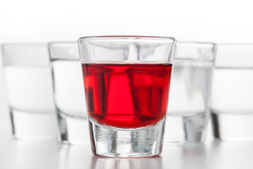 Glasses of alcohol. One red flavoured, the others clean vodka. White background.