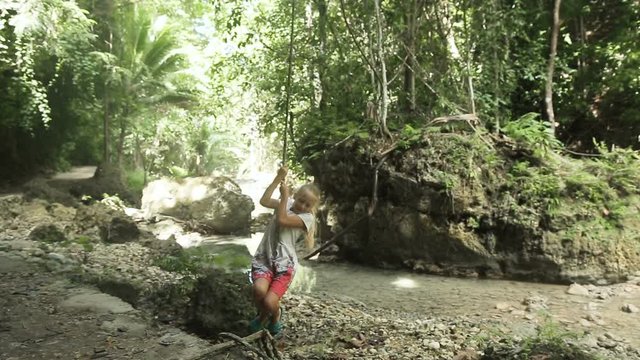 children girls playing hanging and climbing from lianas at the jungle forest park outdoor.young girl playing with a vine in the rain forest near the river.Travel concept.Family,summer vacation.