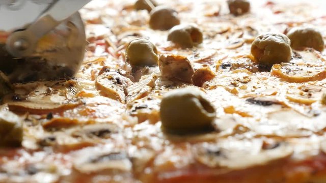 Cutting warm pizza on smaller pieces with roller-knife close-up 4K 2160p UltraHD footage - Warm tasty pizza with cheese and olives on table 4K 3840X2160 30fps UHD video 