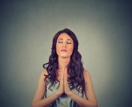 Young woman praying eyes closed isolated on gray wall background