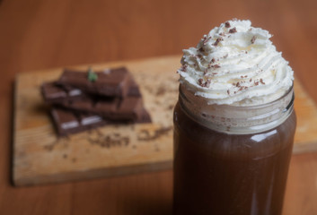 cocoa with whipped cream on a background of a wooden board with chocolate