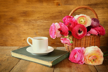 cup of coffee next to old book next to flowers on wooden table