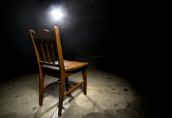 Isolated wooden chair in a dark scary prison with an interrogation spotlight - obrazy, fototapety, plakaty
