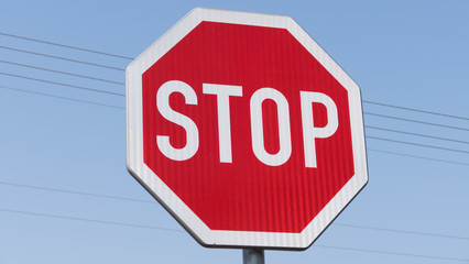 A detail of red road sign STOP in the blue air with electrical wires - color toned image