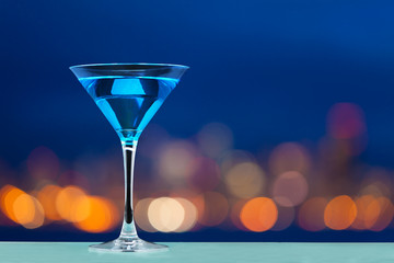 Glass of martini standing against city lights