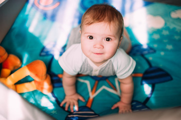Cute little baby boy playing in colorful playpen, indoors. Beautiful child having fun at nursery.