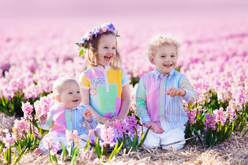 Three children playing in beautiful hyacinth flower field. Little girl, toddler boy and baby play in sunny summer garden with purple flowers. Kids having fun outdoors. Brothers and sister together.