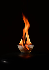 Small transparent glass bowl standing on a black surface with fire blazing in it close up isolated...