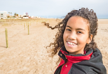 Adorable young girl wearing red coat, walking on beach in Spain in winter. Beautiful brazilian child with long curly hair enjoying wind and sun outside, image for children concept family blog.  - 108079492