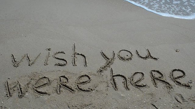 Conceptual wish you were here text handwritten in sand on a beach