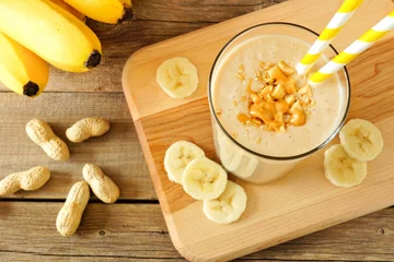 Photo sur Plexiglas Milk-shake Peanut butter banana oat smoothie with paper straws, on a wood board on rustic table, downward view